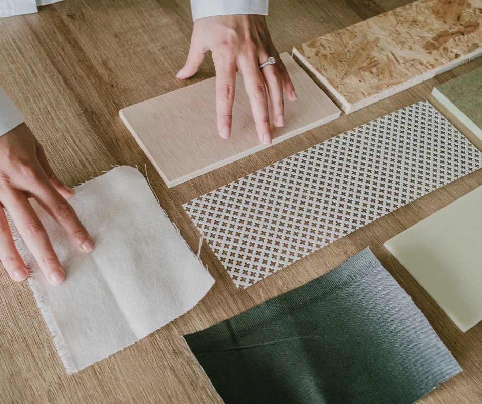 Hands arranging best roofing material samples, including wood, fabric, laminate, and patterned sheets, on a wooden table for a Bay Area home project.